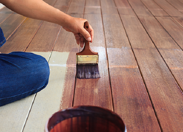 Un uomo sta applicando della vernice per legno a un pavimento in parquet